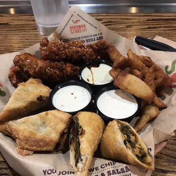Chili's - A basket of fried food items, including spring rolls and onion rings, with three dipping sauces, on a wooden table. - American Near Me - Lafayette, Indiana