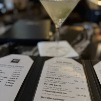 ALC Steaks - DIRTY TINI - A martini glass with a lime wedge on a bar counter, with menus in the foreground and a blurred background. - Steakhouses Near Me - Austin, Texas