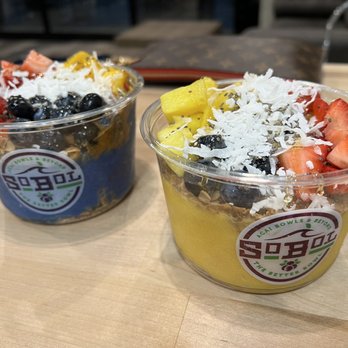 SoBoL - Paired deliciousness!! - Two acai bowls with toppings like strawberries, blueberries, mango, shredded coconut, and granola are placed on a wooden table. - Juice Bars & Smoothies Near Me - Poughkeepsie, New York
