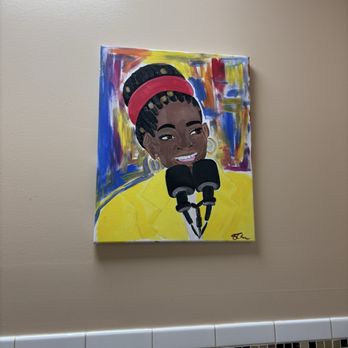 Backyard Barbeque - Artwork in the bathroom - A vibrant painting depicts a woman with braided hair, wearing a red headband and yellow jacket, holding microphones, with an abstract background. - Barbeque Near Me - Freeport, New York