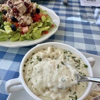 Kelly's Cafe - Thick & creamy clam chowder. - A bowl of thick, creamy clam chowder garnished with chopped herbs, placed on a white plate on a checkered blue tablecloth. - Sandwiches Near Me - Boothbay Harbor, Maine