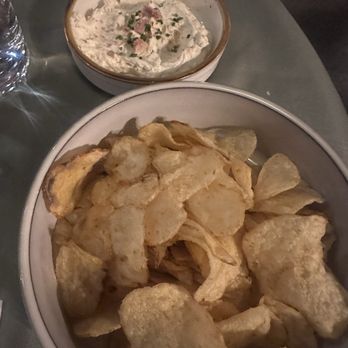 Severo - Amazing Dip!! - A large bowl filled with potato chips and a small bowl of creamy dip with herbs and bacon bits are on a table. - American Near Me - Richfield, Utah