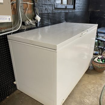 606 Junk Removal - The motor on the deep freezer was blown. - A white chest freezer with a closed lid is positioned against a black brick wall in a utility or storage area. - Junk Removal & Hauling Near Me - Chicago, Illinois