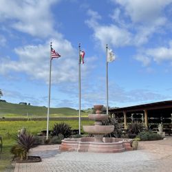 Robledo Family Winery - Green vineyards, blue skies, and flags celebrating the Robledo Family's MX-US heritage.