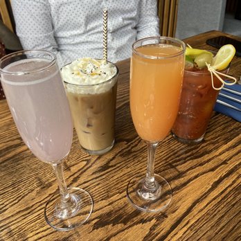 Cloud & Spirits - Drinks - Four cocktails with various colors and garnishes are arranged on a wooden table in a restaurant setting. - New American Near Me - Cambridge, Massachusetts