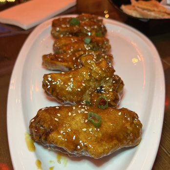 POTS - A white oval plate holds glazed chicken wings topped with sesame seeds and chopped green onions, served in a restaurant setting. - Hot Pot Near Me - Peabody, Massachusetts