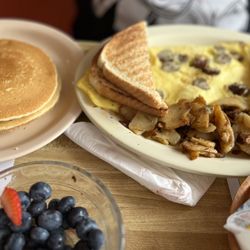 Sunny Hunny by the Sea Family Restaurant & Pancake House - Fruit bowl already eaten banana, blueberries, and strawberries. Sausage omelet with hash browns and toast, pancakes.