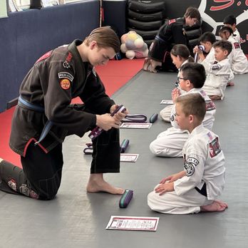 5.0 Evolved Martial Arts - A Jeff Speakman Training Center - Martial arts instructor helps a student with their belt. - Brazilian Jiu-jitsu Near Me - Redlands, California 5.0 Evolved Martial Arts - A Jeff Speakman Training Center - Martial arts instructor helps a student with their belt. - Brazilian Jiu-jitsu Near Me - Redlands, California