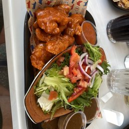 Chicken Tenders - A serving of house-made chicken tenders coated in sauce, accompanied by a side salad with tomatoes, onions, and lettuce, and two small containers of dressing.