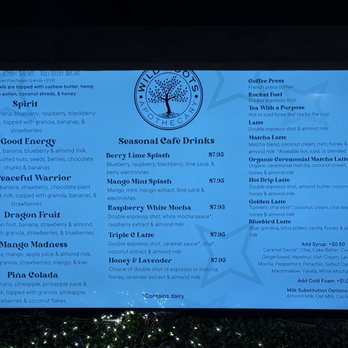 Wild Roots Apothecary - Menu - Digital menu board at Wild Roots Apothecary in Schofield, WI, displaying a variety of seasonal café drinks such as smoothies, lattes, and specialty beverages. The menu includes descriptions, prices, and options for customization, with sections for drinks like Berry Lime Splash, Mango Mint Splash, and Blueberry Latte. The board also features additional options for syrups, cold foam, and milk substitutions, along with allergen information. The background is illuminated, and the menu is organized into categories for easy reading. - Coffee & Tea Near Me - Schofield, Wisconsin