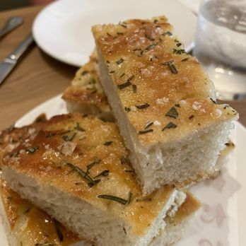 Celeste - Focaccia - Three pieces of focaccia bread with herbs are stacked on a plate, served at a restaurant. - Desserts Near Me - Narragansett, Rhode Island