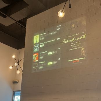 Violet Crown Austin - A digital projection shows movie titles and times on a white brick wall inside Violet Crown Austin, a cinema with modern lighting fixtures. - Cinema Near Me - Austin, Texas
