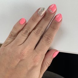 A hand with manicured nails, painted in pink with one nail decorated with glitter and rhinestones, resting on a white surface.