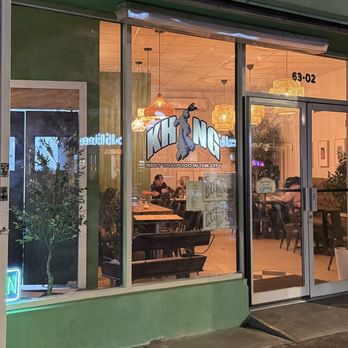 Khing - Exterior - Khing, a Thai restaurant in Queens, NY, has a glass storefront with interior lighting, seating, and decor visible through large windows, including plants and hanging lights. - Thai Near Me - Queens, New York