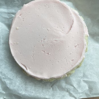 Swig - Sugar cookie - A round sugar cookie with a layer of pale pink icing covering the top surface. The icing appears smooth with minor imperfections and a slightly uneven edge. The cookie is placed on white parchment paper, which is on a flat surface. The image is taken from above, showing the entire cookie and part of the background. - Desserts Near Me - Gilbert, Arizona