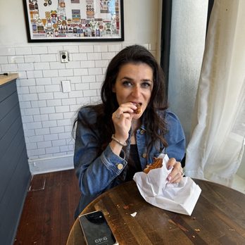 Twisted Grounds - a woman sitting at a table eating a donut - Coffee & Tea Near Me - Philadelphia, Pennsylvania