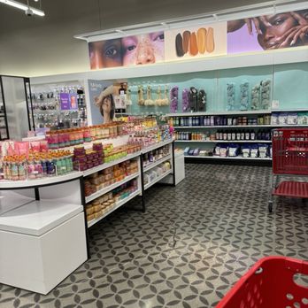 Target - Beauty section - The photo depicts the beauty section of Target in Provo, UT, featuring shelves stocked with skincare products, bath accessories, and beauty supplies. The area has a patterned tile floor, overhead lighting, and a large banner with images of diverse faces and makeup swatches. A red shopping cart is visible in the foreground, and the shelves are organized with various products including jars, bottles, and bath sponges. - Personal Shopping Near Me - Provo, Utah