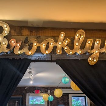 Vineapple - A marquee sign spelling 'Brooklyn' with illuminated bulbs is mounted above a doorway with black curtains, inside a venue. - Italian Near Me - Brooklyn, New York