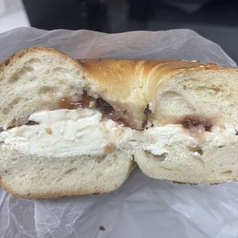 Springtree Bagels - A bagel cut in half reveals a filling of cream cheese and jelly. The bagel has a golden-brown crust and a soft interior. It is placed on a piece of parchment paper, with a blurred background that suggests an indoor setting. - Bagels Near Me - Englewood, New Jersey
