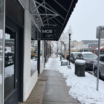 MOB Coffee - The image shows a snow-covered sidewalk outside MOB Coffee, with parked cars, street lamps, and benches along the street. - Coffee & Tea Near Me - Denver, Colorado
