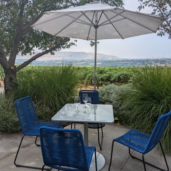Hightower Cellars - a patio with blue chairs and an umbrella - Wineries Near Me - Benton City, Washington