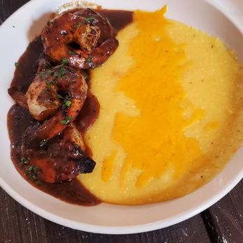 Flamingobaby Kitchen - A dish featuring mashed potatoes topped with melted cheddar cheese and served alongside shrimp in a dark sauce. - Caribbean Near Me - Brooklyn, New York