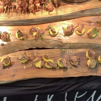 Copper State Kitchen - Short rib and polenta cakes - Slices of cooked beef with green garnish are displayed on two wooden serving boards at a catering event. The boards are placed on a black tablecloth, with business flyers or promotional cards positioned to the side. The presentation emphasizes a rustic style, with the natural wood serving trays and garnished meat slices arranged in a pattern. - Personal Chefs Near Me
