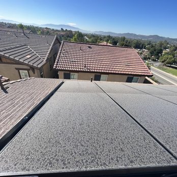 Clear Choice Cleaning - The image captures a high-angle view of multiple residential rooftops, including tile and shingle roofs, with a clear blue sky overhead. Distant mountains and greenery are visible in the background, indicating a suburban or semi-rural area. The photo appears to be taken from a rooftop or elevated position, with sunlight illuminating the scene. - Solar Panel Cleaning Near Me