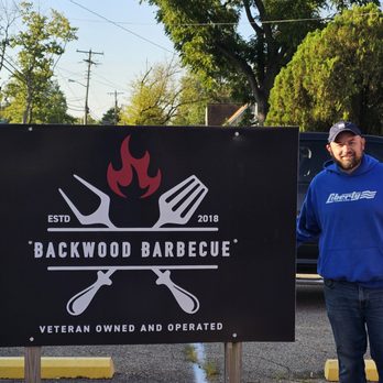 Backwood Barbecue - a man standing in front of a sign - Barbeque Near Me - Fillmore, Indiana Backwood Barbecue - a man standing in front of a sign - Barbeque Near Me - Fillmore, Indiana