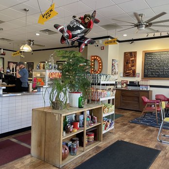 Darwin - Fun interior - A small airplane model with a monkey figure is suspended from the ceiling of a cafe, with signs indicating 'Pick Up' and 'Order' nearby. - Sandwiches Near Me - Syracuse, New York