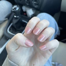 A person's hand with shiny, pinkish nail polish is visible inside a car, with the background showing the vehicle's interior and gear shift.