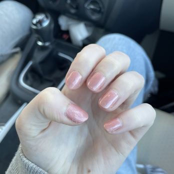 Crystal Nails - A person's hand with shiny, pinkish nail polish is visible inside a car, with the background showing the vehicle's interior and gear shift. - Nail Salons Near Me - Bridgewater, Massachusetts