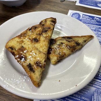 Annie's Overflow - Raisin bread French toast - Two slices of raisin bread French toast dusted with powdered sugar on a white plate, set on a wooden table. - Breakfast & Brunch Near Me - Holderness, New Hampshire