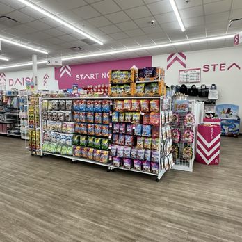 Daiso - Shelves stocked with assorted snack bags, including chips and candies, are positioned in the interior of a Daiso store in Mesa, AZ. The store features a pink and white color scheme with signage indicating sections like 'START NOW' and 'Daiso.' The ceiling has fluorescent lighting, and the floor is covered with wood-patterned vinyl. Additional store items, such as bags and accessories, are visible in the background. - Department Stores Near Me - Mesa, Arizona