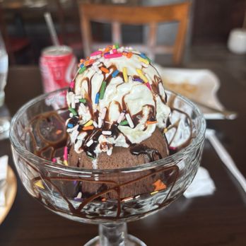 Monkey Thai Diner - Lava cake - A glass bowl contains chocolate ice cream topped with whipped cream, colorful sprinkles, and drizzled with chocolate syrup, set on a wooden table. - Thai Near Me - Clark, New Jersey