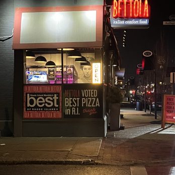 Bettola - Nighttime view of Bettola restaurant's exterior, featuring neon signs and window display with interior lighting, located on a city sidewalk. - Pizza Near Me - Cranston, Rhode Island