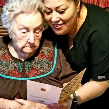 Grandmother's House - 100 year-old, Miss Betty being read a card from a friend by her attendant Maria. - Assisted Living Facilities Near Me - Arlington, Texas Grandmother's House - 100 year-old, Miss Betty being read a card from a friend by her attendant Maria. - Assisted Living Facilities Near Me - Arlington, Texas