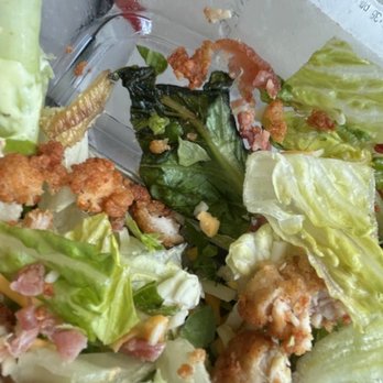 Chick-fil-A - Not what you 've come to know as Chick-Fil-A quality?  Big oops! - A close-up image of a salad featuring various types of lettuce, bacon bits, and fried chicken pieces. The salad appears to be partially eaten, with some dressing and crumbs visible on the ingredients. The background shows a clear container and some reflective surfaces, indicating it was served in a takeout or casual dining setting. - Salad Near Me - Flint, Michigan