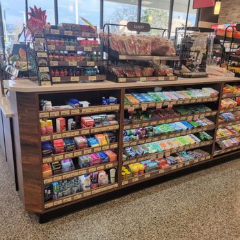 Wawa - Counter area - Checkout counter at a grocery store featuring snacks, baked goods, and health products on wooden shelves, with large windows and self-checkout sign in the background. - Gas Stations Near Me - Glenside, Pennsylvania