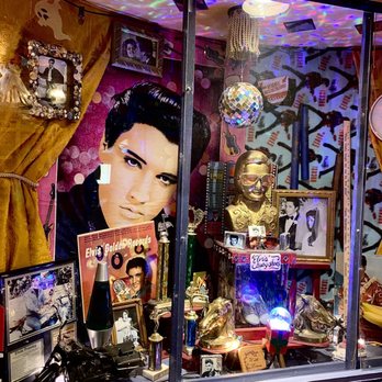 Chuy's - Elvis memorial... Elvis had a house near here when he was in basic training - The display window showcases Elvis Presley memorabilia, including framed photographs, a large portrait of Elvis, gold records, and various decorative items such as a disco ball, gold shoes, and a bust of Elvis. The background has a pink and purple theme with musical and dance-themed decorations, and the window is partially covered with gold curtains. The display appears to be a tribute to Elvis Presley, with various collectibles and memorabilia arranged inside. - Tex-Mex Near Me - Waco, Texas