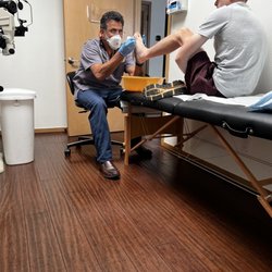 Poipu Mobile MD Clinic - The dr trying to get spines out of his foot from the sea urchin.