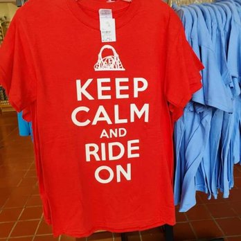 Character Central - A red T-shirt with white text reading 'Keep Calm and Ride On' is displayed on a hanger in a retail store, with blue shirts visible in the background. - Souvenir Shops Near Me - Hershey, Pennsylvania