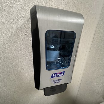 CVS Pharmacy - A wall-mounted Purell hand sanitizer dispenser made of stainless steel with a transparent window is attached to a textured wall. The dispenser has a label reading 'Purell Healthy Soap' and a black push button at the bottom for dispensing soap or sanitizer. The setting appears to be a public restroom or similar facility. - Drugstores Near Me - Peekskill, New York