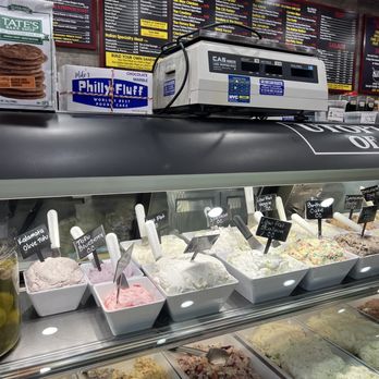Utopia Bagels - Cream cheese - The image shows a selection of ice cream flavors in bowls behind a glass display case at an ice cream shop. Each flavor has a small sign with its name, such as kalamata olive, toffee blueberry, and birthday cake. The shop has a menu board in the background listing food options, and a cash register is visible on the counter. The setting appears to be a casual dessert shop with a variety of ice cream options. - Bakeries Near Me - Whitestone, New York