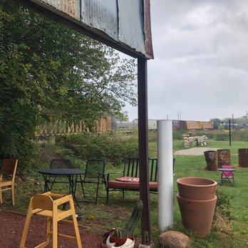 Lockwood Cafe - An outdoor seating area with various chairs and tables, including a high chair, is situated near a grassy field and train tracks. - Cafes Near Me - Ames, Iowa