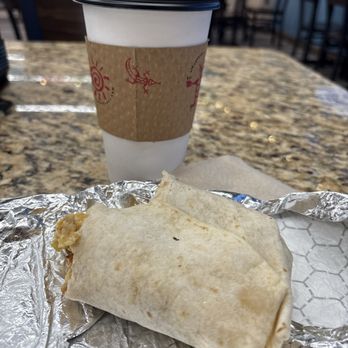 Route 66 Lounge - A disposable coffee cup with a black lid and a cardboard sleeve is placed on a granite table, with a burrito wrapped in a flour tortilla on aluminum foil in the foreground. - Sports Bars Near Me - Albuquerque, New Mexico