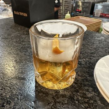 Bonfire Grill - Smoked old-fashioned - A cocktail with an amber hue and a lemon peel garnish is placed on a dark granite bar counter in a restaurant setting. - New American Near Me - Tomball, Texas