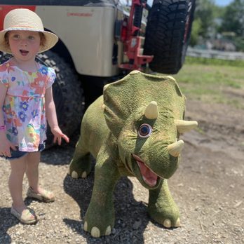 KC Pumpkin Patch - A girl wearing a floral dress and sun hat stands outdoors beside a rhinoceros-shaped statue with a large eye and open mouth, near a large vehicle. - Pumpkin Patches Near Me - Olathe, Kansas