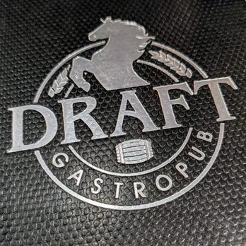 Draft Gastropub - The image shows a close-up of a textured black surface, likely a mat or surface of a bag, with a metallic logo embossed on it. The logo includes a horse silhouette at the top, the word 'DRAFT' in large letters, and a small barrel icon beneath the text. Surrounding the logo are the words 'GASTROPUB,' suggesting branding for Draft Gastropub, a modern gastropub offering diverse cuisine and craft beverages. - Gastropubs Near Me - Appleton, Wisconsin