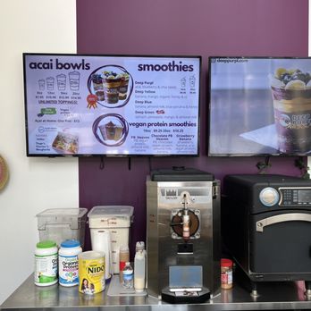 Deep Purpl - a coffee machine and a menu on a wall - Two digital menu screens show acai bowls, smoothies, and vegan protein options at a vegan-focused acai shop. - Acai Bowls Near Me - Chicago, Illinois